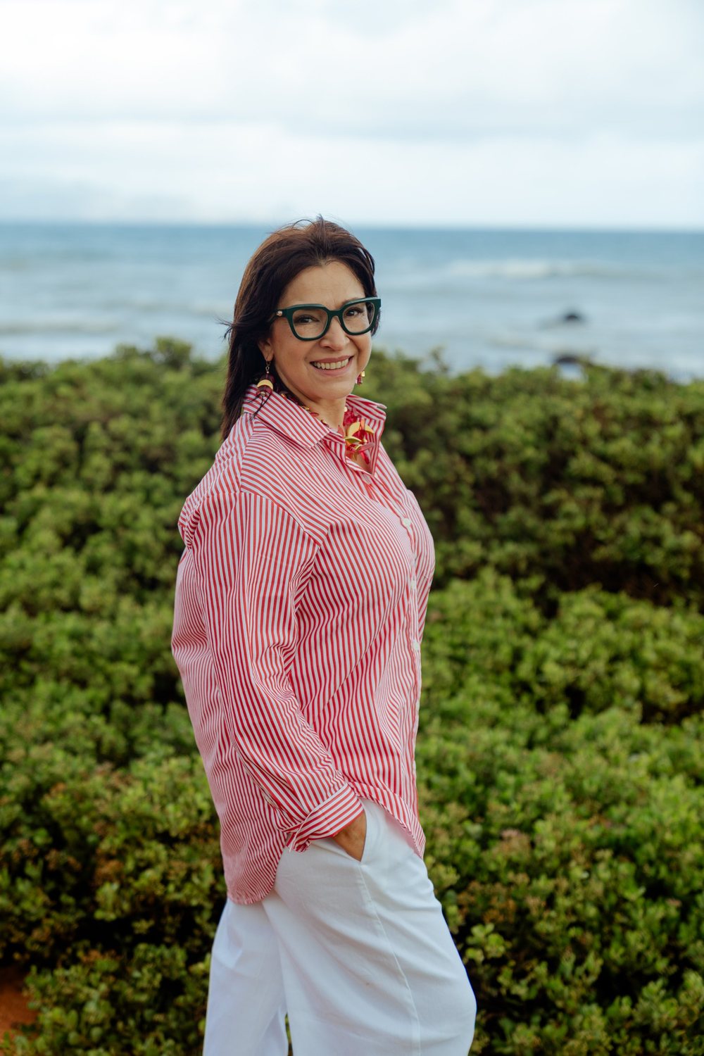 Sandra Gat sonriendo frente al mar, con camisa de rayas y lentes verdes